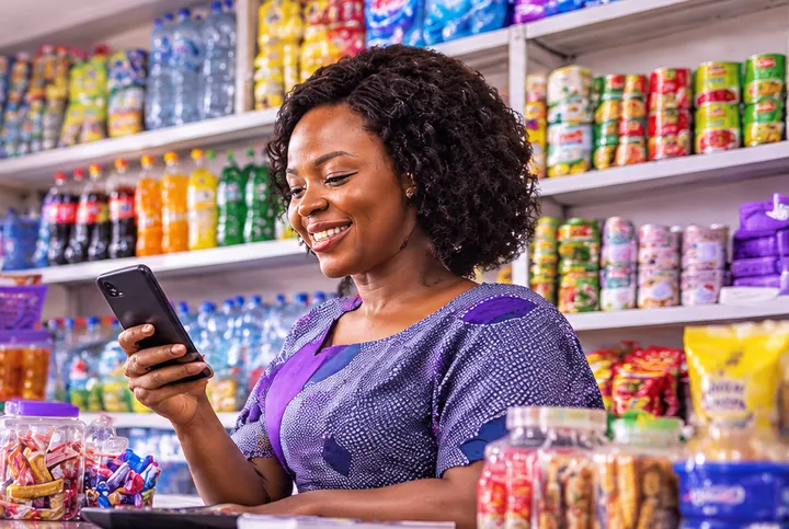 Une commerçante sourit en consultant son téléphone au comptoir de sa boutique.